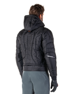 Veste imperméable Alpinestars Mohobbs, noire, vue arrière montrant la construction matelassée et rembourrée, une capuche, le mot-symbole astars vertical au dos et le marquage Alpinestars sur les manches, portée avec un pantalon gris et des gants noirs.