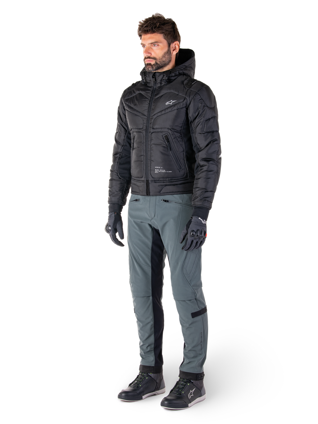 Veste Mohobbs Waterproof Alpinestars, noire, blouson aviateur de moto urbain matelassé avec capuche, portée par un mannequin avec un pantalon de moto gris et des gants noirs, avec un logo blanc sur la poitrine, équipement de protection moderne d'inspiration streetwear