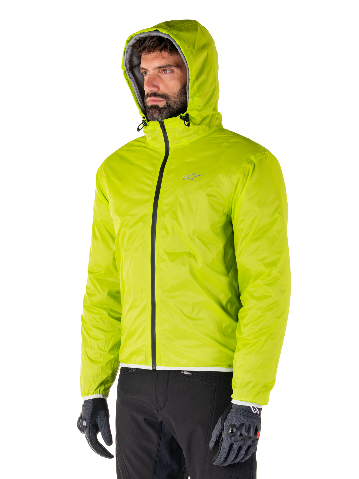 Veste imperméable Alpinestars Mohobbs, doublure de pluie compressible Lime Punch, veste à capuche vert néon éclatant portée avec un pantalon noir et des gants gris, équipement de moto d'inspiration streetwear urbain