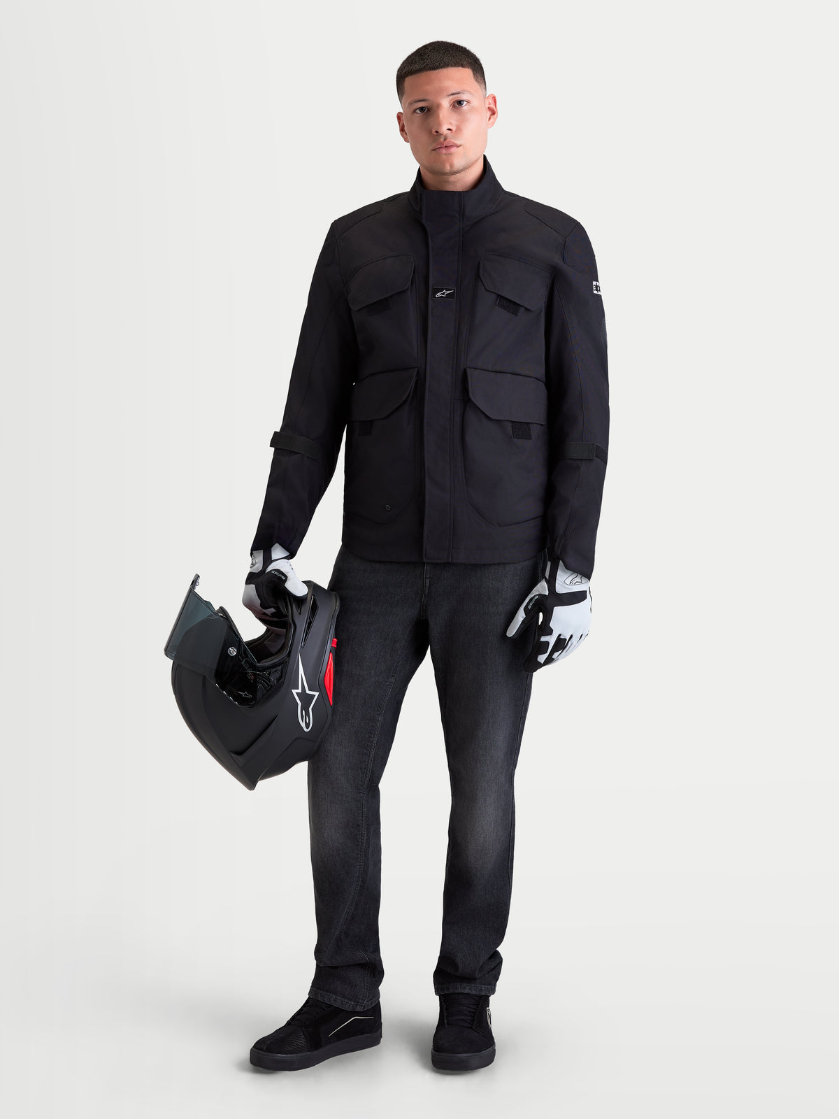 Alpinestars Altan Drystar Jacket, men's urban contemporary motorcycle jacket in black, front view on a model holding a helmet and wearing riding gloves, waterproof textile utility jacket with cargo pockets