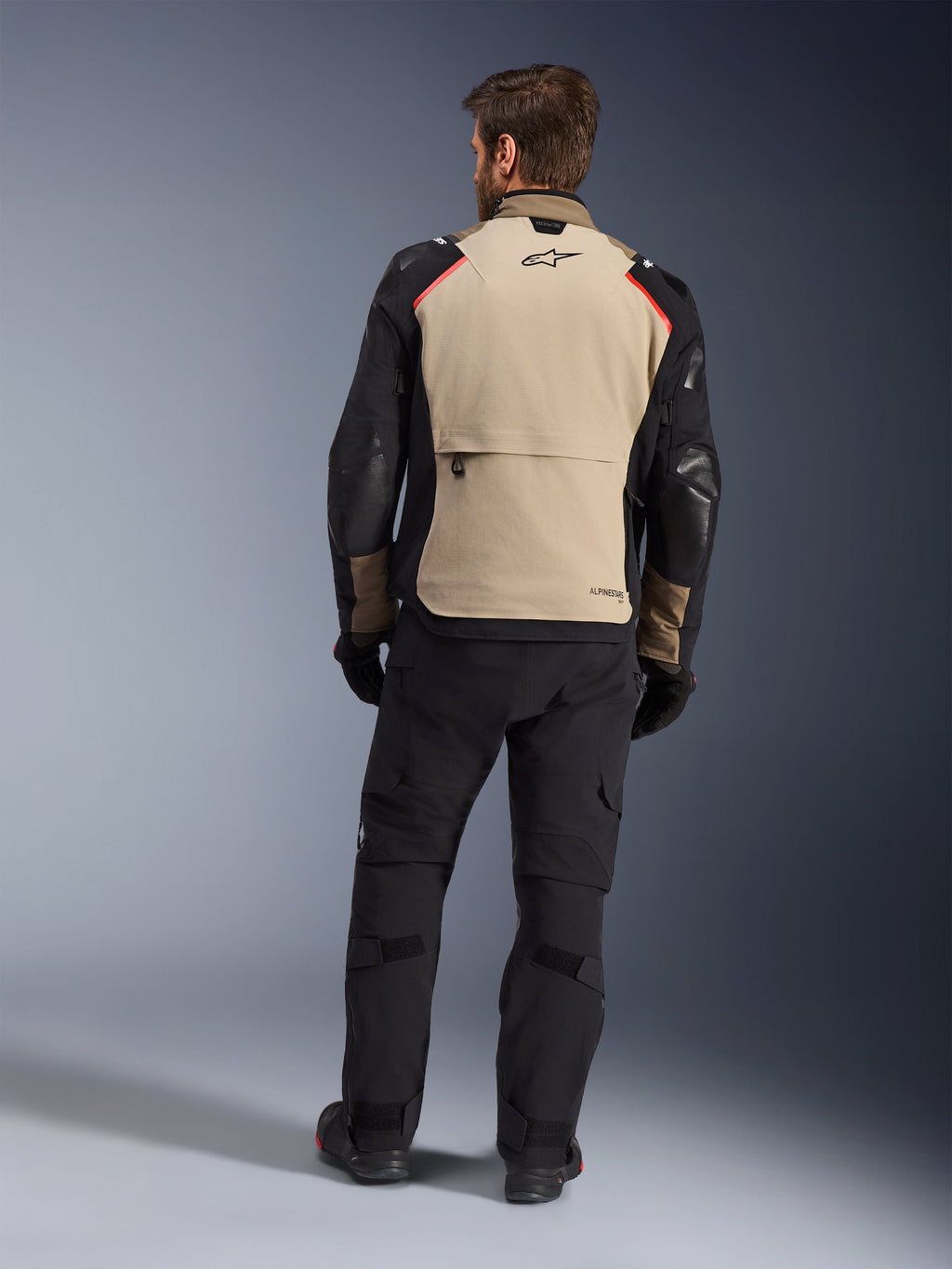 Veste Alpinestars Andes Pro Drystar® XF, Walnut Aluminum, vue de dos, veste de moto d'aventure avec manches noires et accents rouges aux épaules, portée avec un pantalon de moto et des gants noirs.