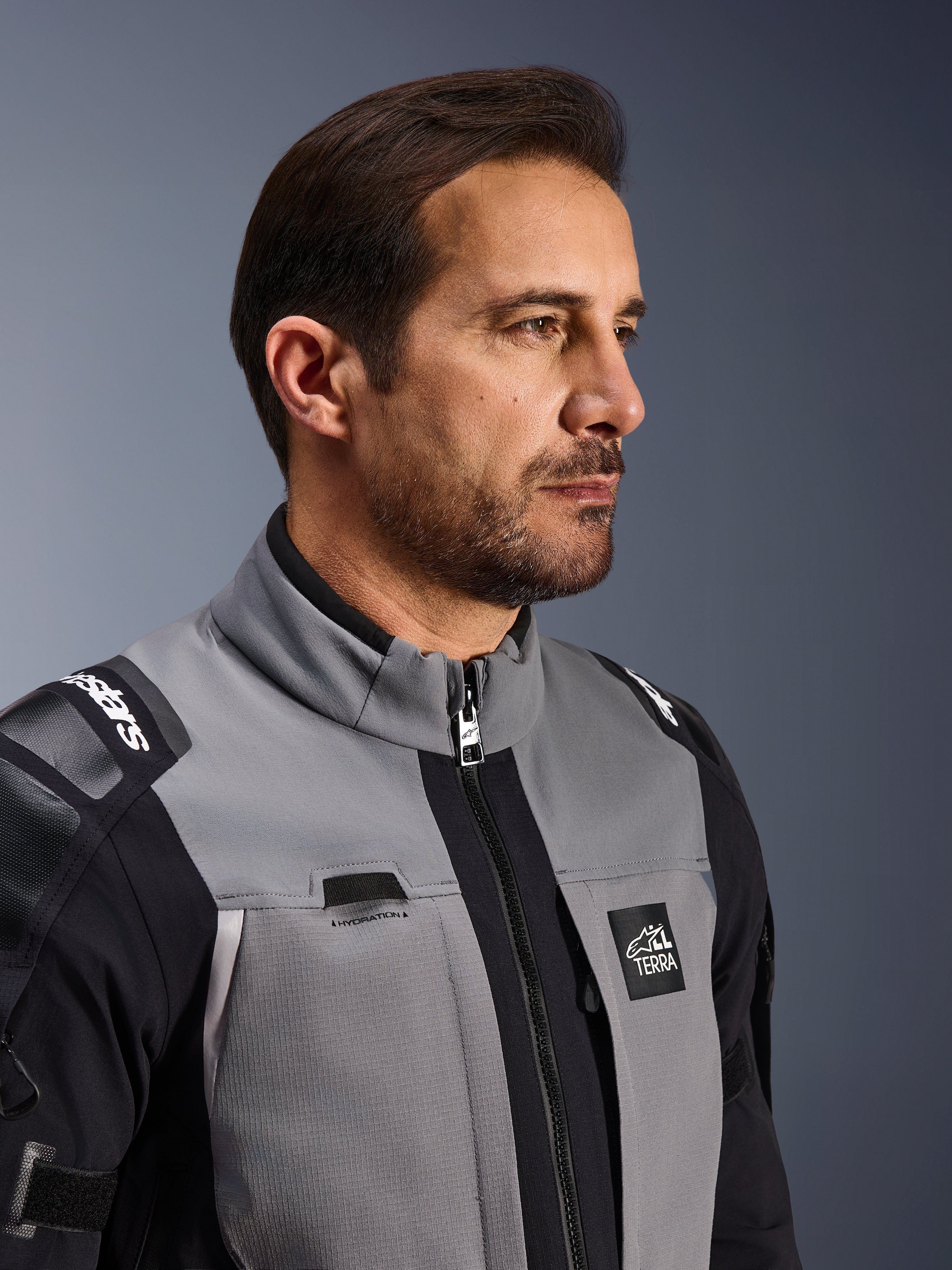 Veste Alpinestars Andes Pro Drystar® XF, veste de moto d'aventure, gris foncé et noir, gros plan sur le buste et le col, présentant le marquage Terra et le détail du passage pour tube d'hydratation, portée par un homme en studio
