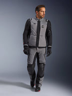Modèle masculin portant la veste Alpinestars Andes Pro Drystar® XF en gris foncé et noir, tenue de moto aventure avec pantalon et gants assortis, dotée d'une coque technique en textile avec marquage « All Terra », équipement complet pour le touring d'aventure longue distance.