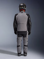 Veste Alpinestars Andes Pro Drystar® XF, vue arrière, équipement de touring aventure gris foncé et noir, porté avec un pantalon gris et noir assorti, un casque en fibre de carbone noir et des gants noirs, avec panneaux techniques et marquages réfléchissants