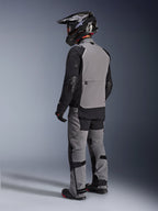 Veste Alpinestars Andes Pro Drystar® XF, veste de moto d'aventure, gris foncé et noir, vue arrière montrant le panneau dorsal gris et les manches noires, portée avec un pantalon assorti et un casque noir, équipement de conduite technique toutes saisons