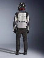 Motorcycle rider seen from behind wearing the Alpinestars Cusco Drystar® Jacket in Ice Gray, Mid Gray, and Deep Gray, featuring a large back ventilation panel and Alpinestars branding, paired with black riding pants and a black helmet, adventure touring motorcycle apparel