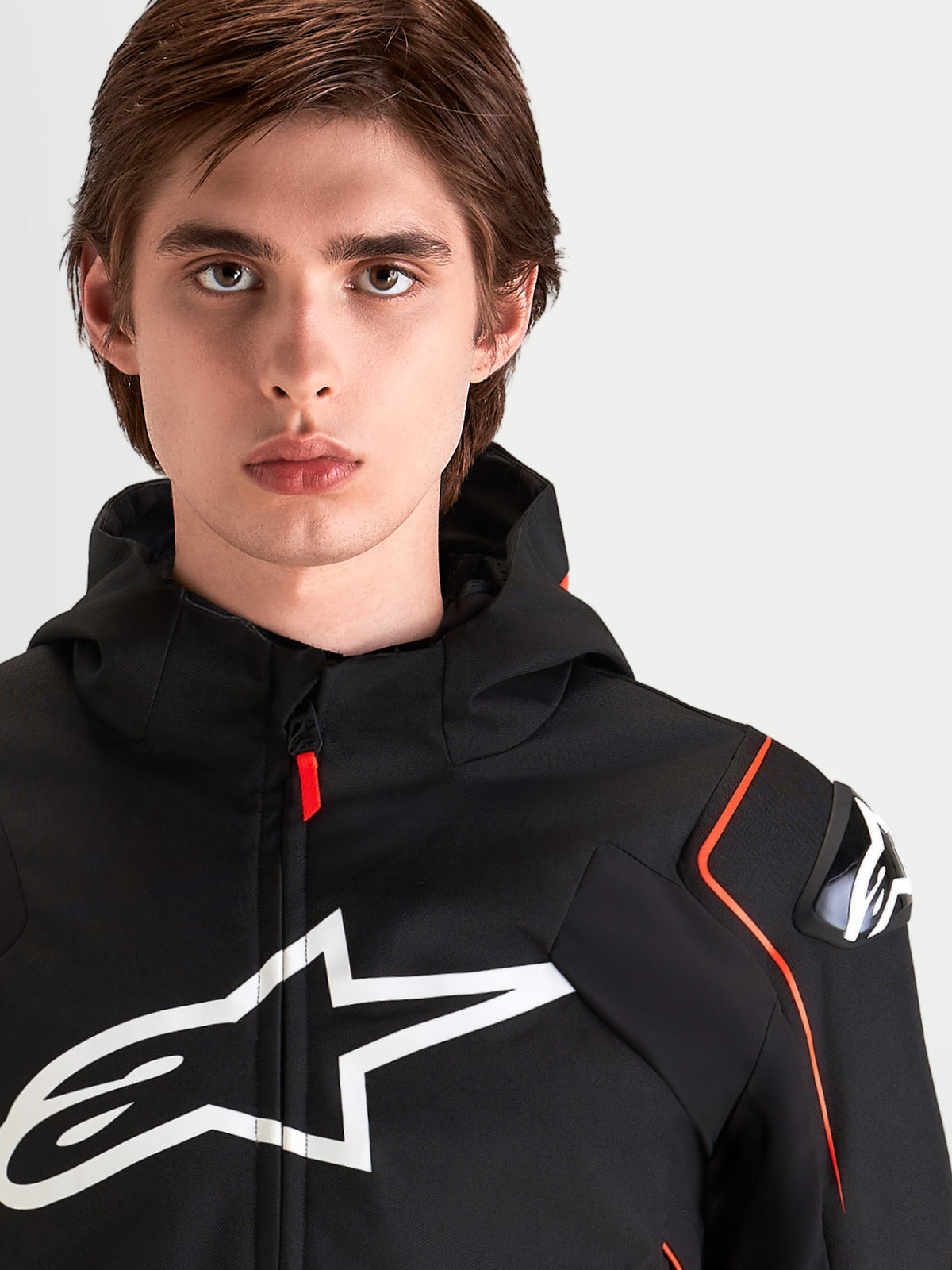 Alpinestars Zaca V2 Waterproof Veste, blouson de moto sport imperméable pour homme, noir et rouge fluo, avec protections d'épaules DFS et grand logo sur la poitrine, portrait rapproché d'un pilote