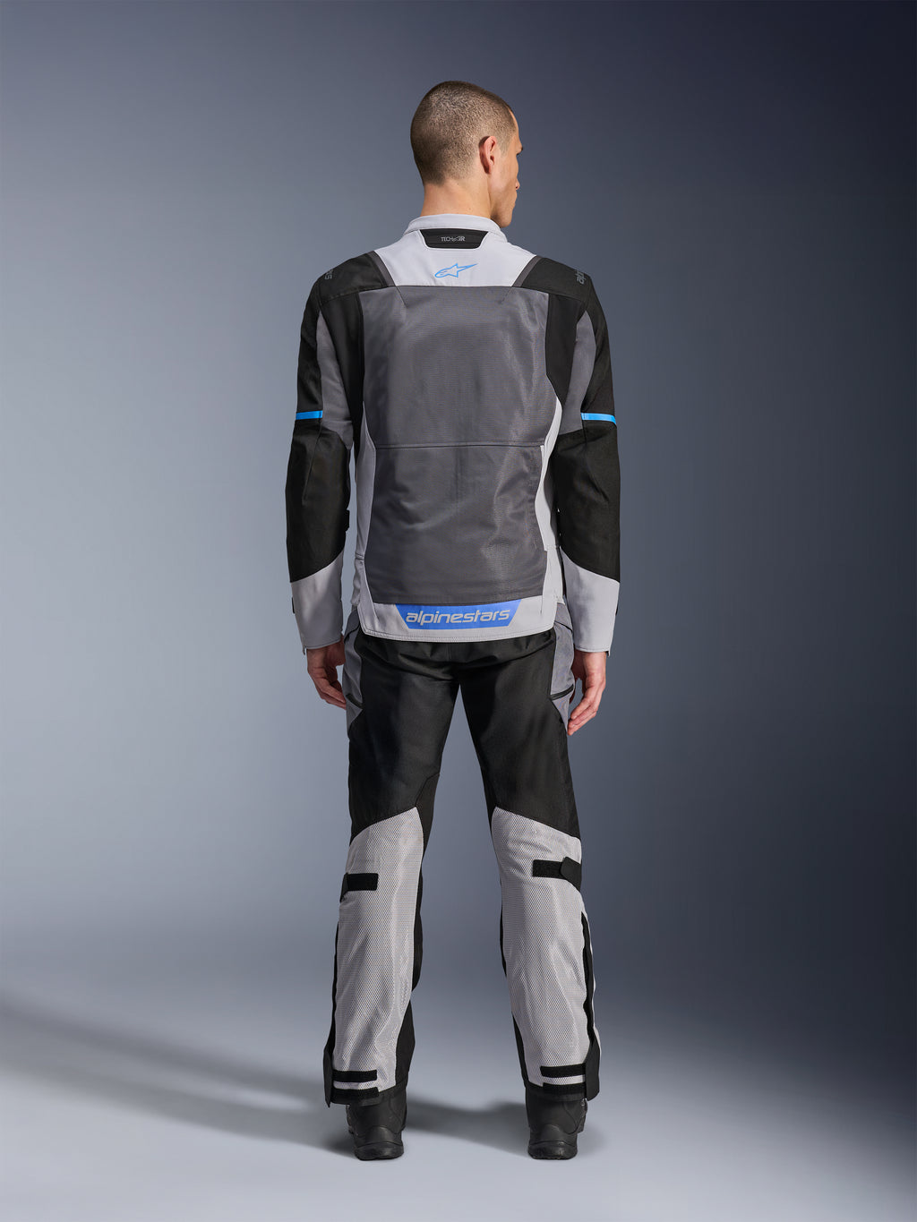 Alpinestars ST-2 Air Jacket, Ice Gray Dark Gray Black, rear view on model, featuring large mesh ventilation panels, blue accents and Alpinestars logo, paired with matching motorcycle pants for adventure touring.