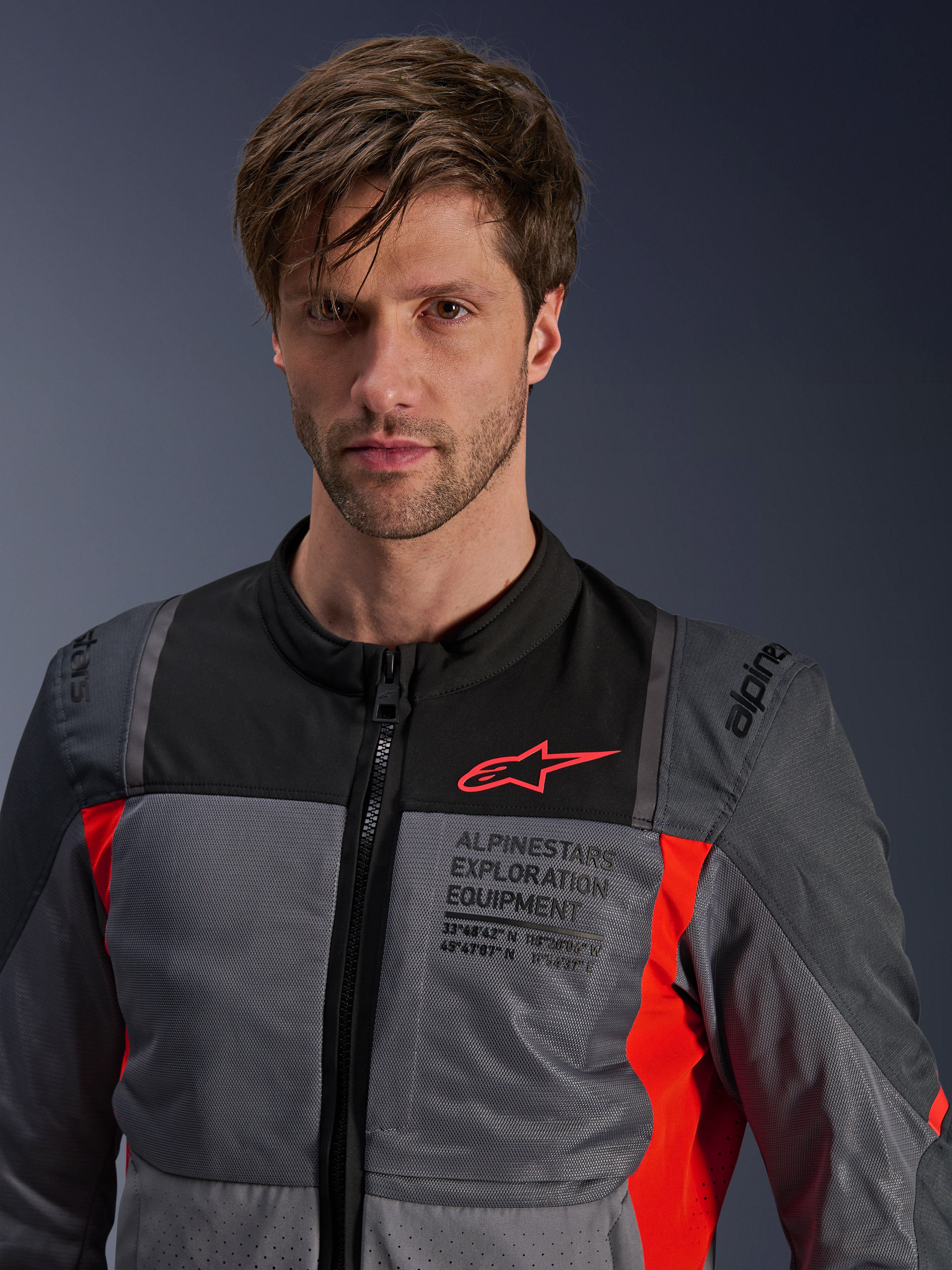 Veste Alpinestars ST-2 Air, Gris Profond, Gris Foncé et Rouge Vif, veste de moto touring d'été portée par un mannequin, dotée de panneaux de ventilation en mesh, logo Astars rouge et marquage « Exploration Equipment » sur la poitrine