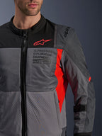 Veste Alpinestars ST-2 Air, veste moto en textile, gris foncé et gris anthracite avec détails rouge vif, gros plan présentant des panneaux en mesh respirant, du tissu perforé au laser et un logo étoile rouge avec marquage Alpinestars Exploration Equipment.