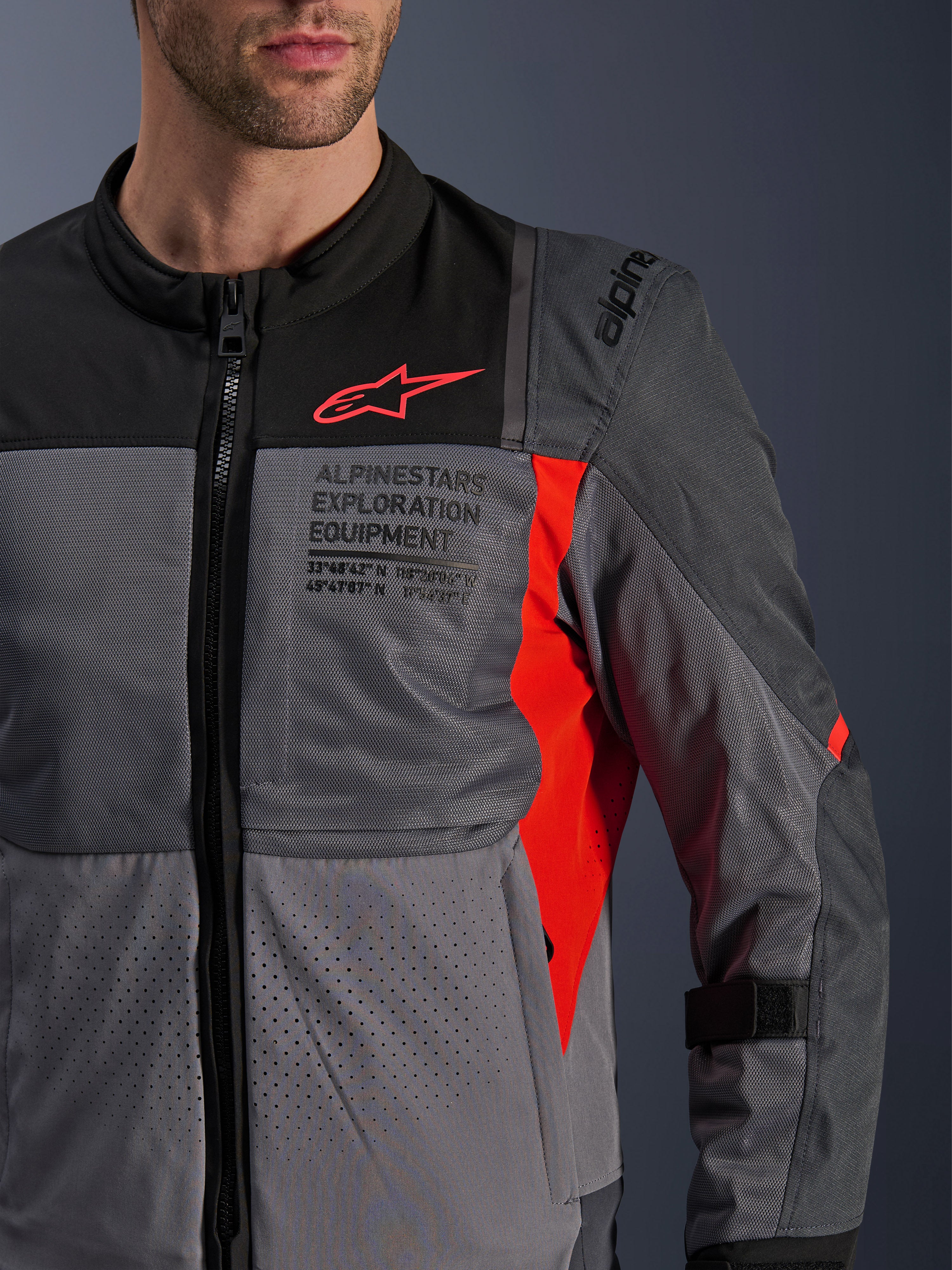 Veste Alpinestars ST-2 Air, veste moto en textile, gris foncé et gris anthracite avec détails rouge vif, gros plan présentant des panneaux en mesh respirant, du tissu perforé au laser et un logo étoile rouge avec marquage Alpinestars Exploration Equipment.