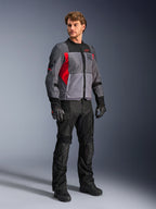 Mannequin homme portant la veste Alpinestars ST-2 Air, veste de moto textile, gris profond, gris foncé et rouge vif, associée à un pantalon, des gants et des bottes noirs, avec de larges panneaux en maille, le marquage Alpinestars Exploration Equipment et une esthétique touring moderne