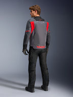 Motard vu de dos portant la veste Alpinestars St-2 Air en gris foncé, gris anthracite et rouge vif, mettant en valeur le grand panneau de ventilation en mesh à l'arrière et les marquages rouges, assortie d'un pantalon de moto noir et de gants gris.