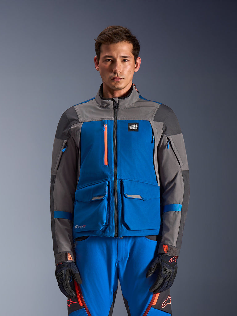 Alpinestars Maxdura Drystar XF Laminated Armored Shell, veste de moto touring pour homme, bleue et grise avec accents orange, imperméable, respirante, poches multiples, col haut, portée avec pantalon assorti bleu à détails noirs et rouges, gants noirs