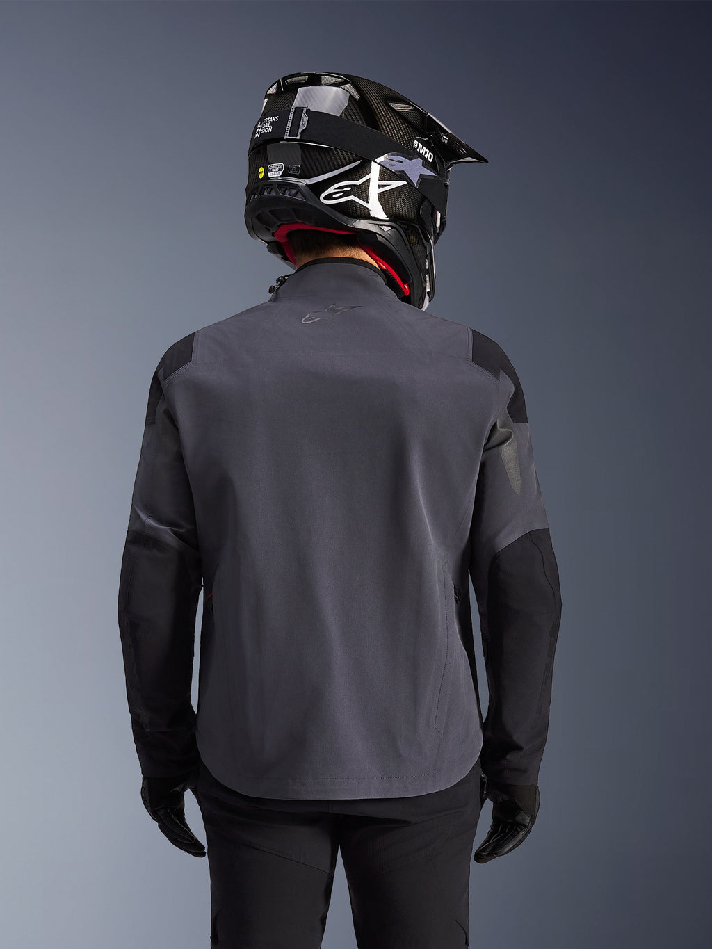 Maxdura Drystar®XF Laminated Armored Shell, Adventure Motorcycle Jacket, Deep Gray Black, rear view showing the technical textile construction and reinforced panels, worn with a black carbon fiber helmet, black riding pants, and gloves