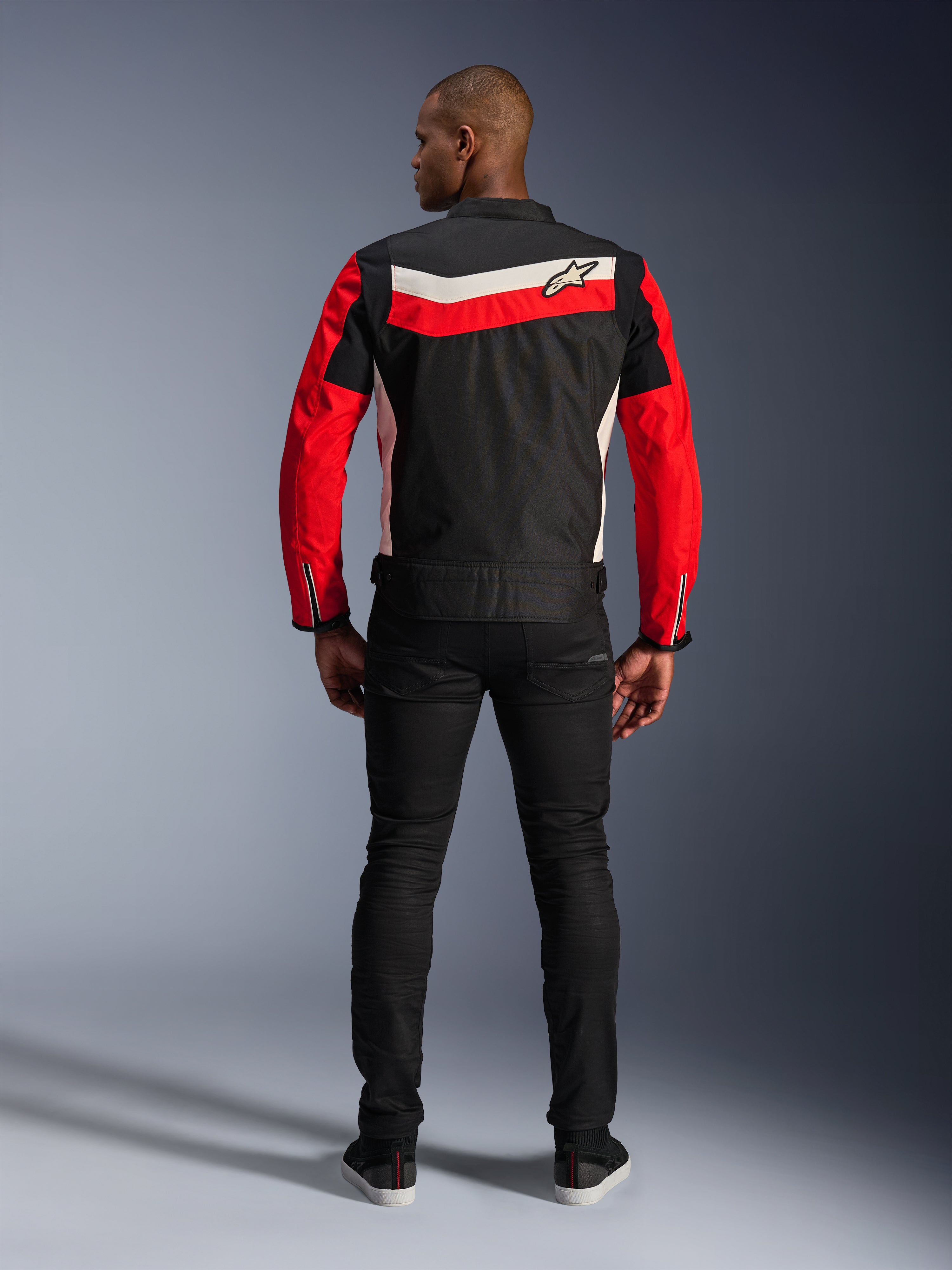 Veste Alpinestars T-Dyno WR, veste de moto en textile, Noir Rouge Vif et Écru, vue de dos montrant des bandes horizontales et des manches rouges, coupe biker d'inspiration vintage, portée avec un pantalon noir, équipement de route urbain
