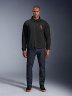 Veste Alpinestars Revved WR noire, portée par un mannequin avec un jean bleu foncé et des baskets noires, vue de face, dotée d'une fermeture par boutons-pression et d'un logo brodé en 3D sur la poitrine, équipement de moto urbain contemporain.