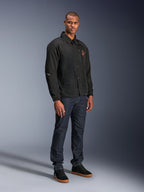 Veste Alpinestars Revved WR en noir, veste de moto urbaine style coach portée par un mannequin avec un jean bleu foncé et des baskets noires, dotée d'une fermeture à boutons-pression et d'un logo brodé, design minimaliste et sportif pour la conduite sur route.
