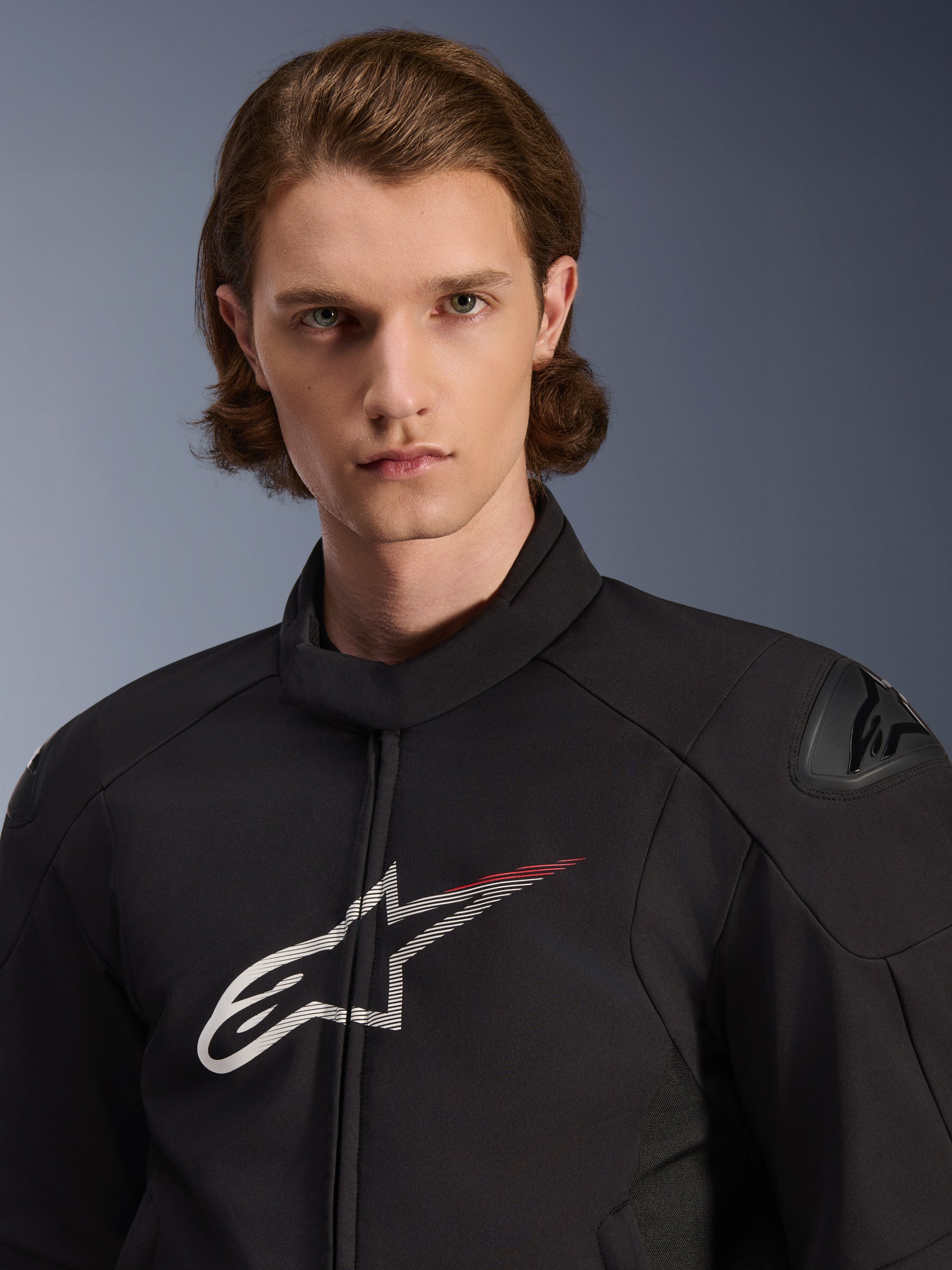 Mannequin portant la veste imperméable Alpinestars SMX, noire avec des accents blancs et rouge vif, avec un grand logo étoile blanc et une traînée rouge sur la poitrine, des protections d'épaules DFS Lite et une construction textile élégante pour la performance à moto sur route.