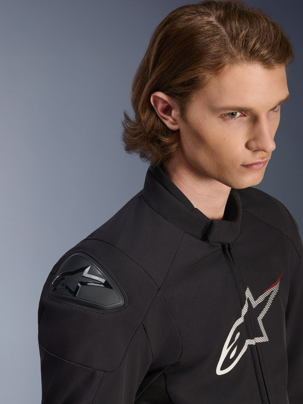 Veste imperméable Alpinestars SMX, noire avec accents blancs et rouges, plan rapproché sur un mannequin masculin, équipée de sliders d'épaule externes DFS Lite et d'un grand logo étoile sur la poitrine, vêtement de moto de sport