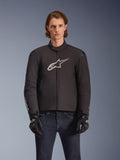 Alpinestars SMX Waterproof Jacket, veste de moto en textile noir avec logo étoile blanc et rouge sur la poitrine, portée par un mannequin avec des gants noirs et un jean bleu, dotée de sliders d'épaule externes et d'une coupe sportive.