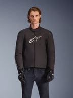 Alpinestars SMX Waterproof Jacket, veste de moto en textile noir avec logo étoile blanc et rouge sur la poitrine, portée par un mannequin avec des gants noirs et un jean bleu, dotée de sliders d'épaule externes et d'une coupe sportive.