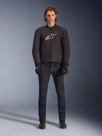 Modèle portant la veste imperméable Alpinestars SMX en noir avec logo blanc et rouge, associée à un pantalon de moto en denim foncé, des gants noirs et des bottes de moto, tenue de moto sportive pour toutes les conditions météorologiques.