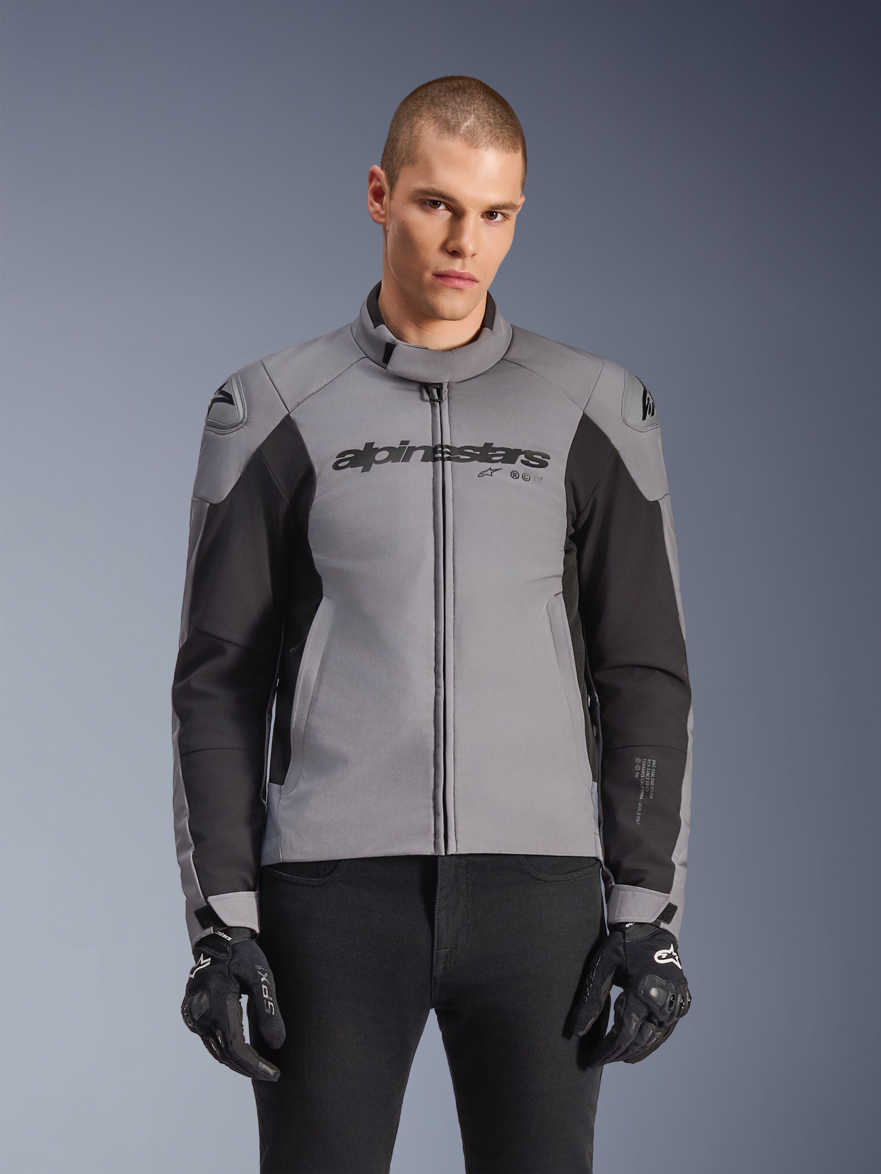 Alpinestars SMX Waterproof Jacket, Sport Road Motorcycle Jacket, Dark Gray and Black, featuring a high collar and DFS Lite shoulder sliders, worn with black SMX gloves, sleek athletic fit for all-weather riding