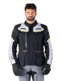 Homme portant une veste Alpinestars Bogotá Pro Drystar®, noir, gris glacé et jaune fluo, veste de moto touring aventure toutes saisons, conception imperméable avec plusieurs poches et marquage vertical, associée à des gants noirs et un pantalon de moto gris