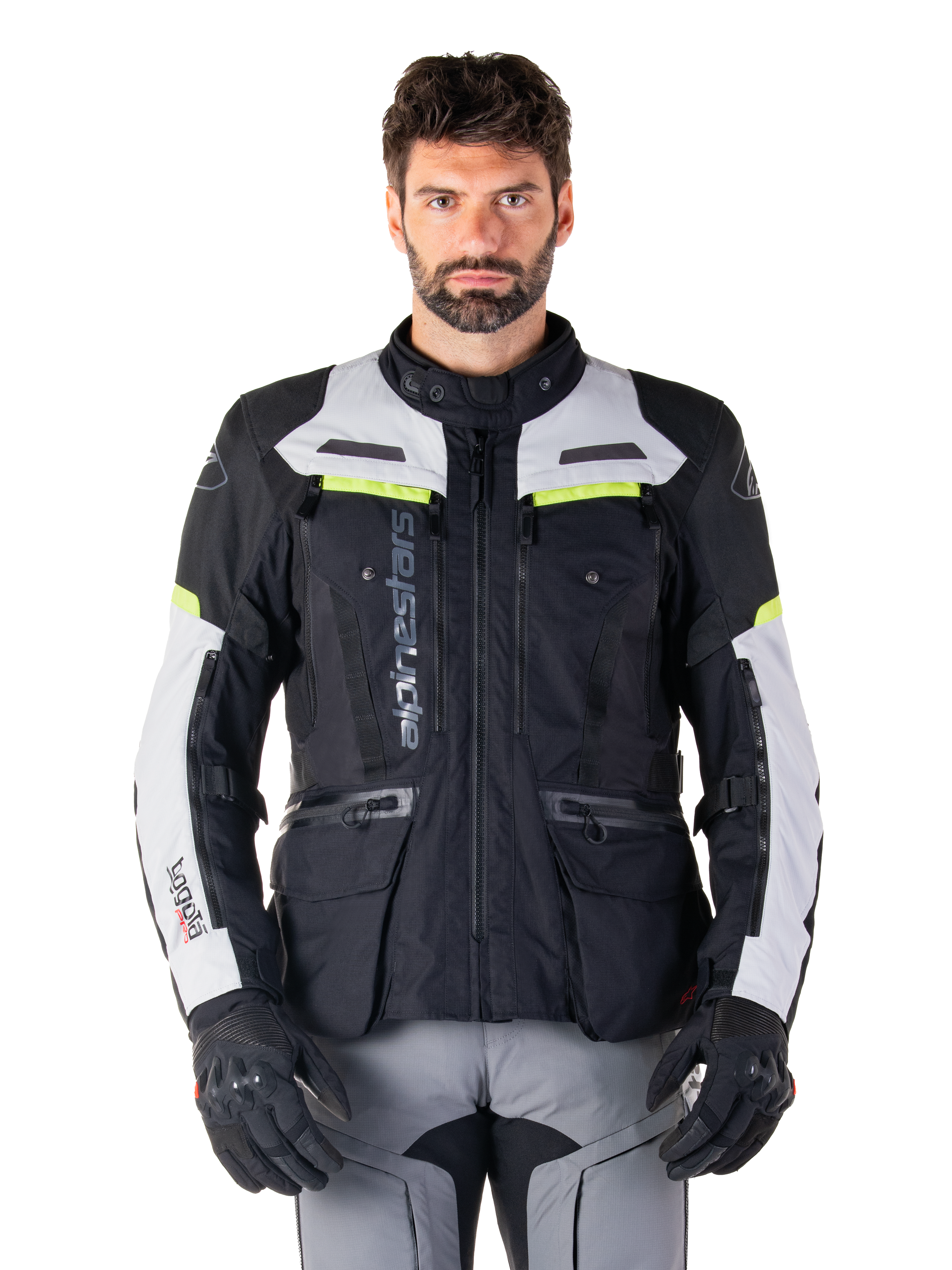 Homme portant une veste Alpinestars Bogotá Pro Drystar®, noir, gris glacé et jaune fluo, veste de moto touring aventure toutes saisons, conception imperméable avec plusieurs poches et marquage vertical, associée à des gants noirs et un pantalon de moto gris