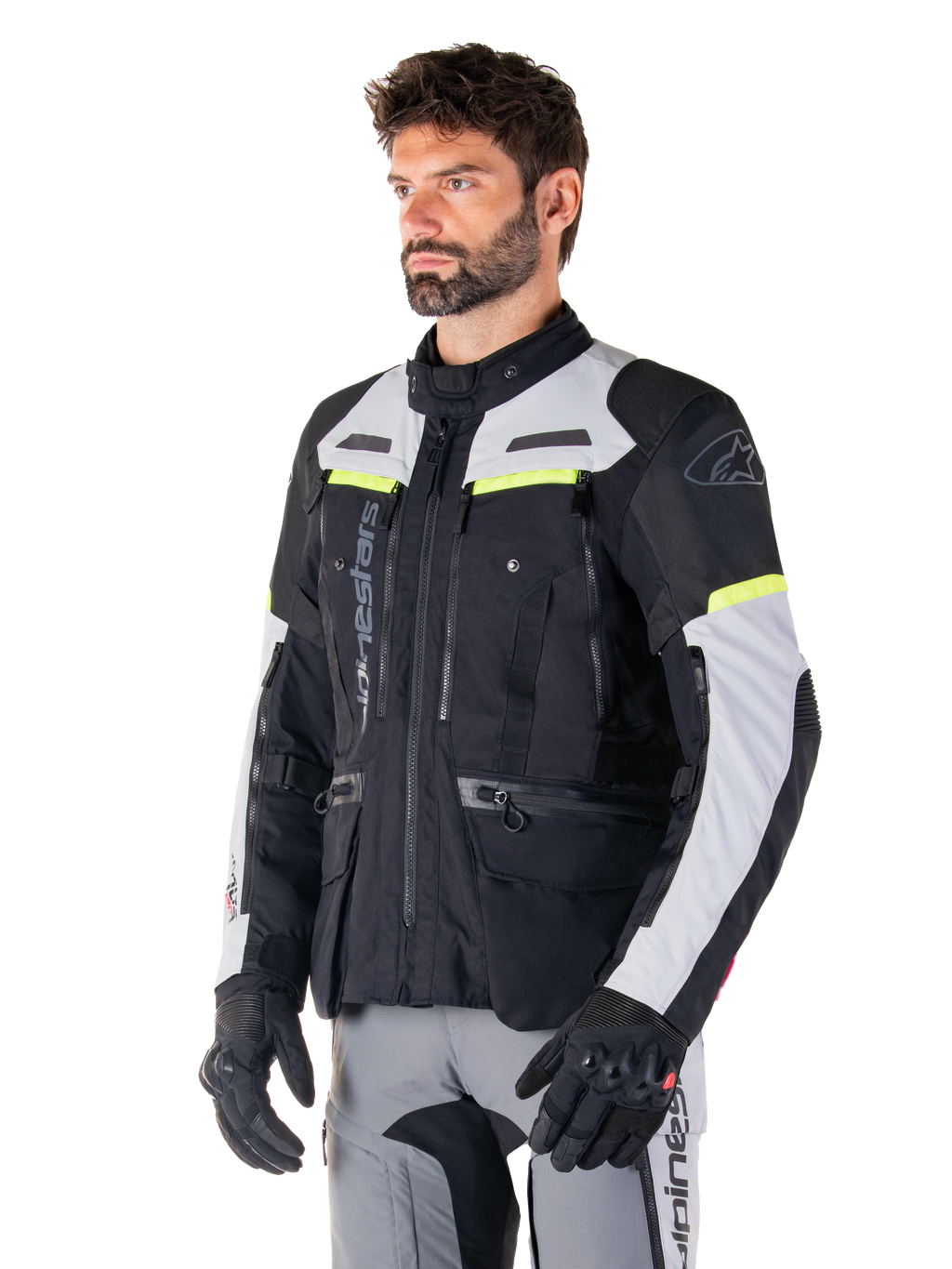 Veste Alpinestars Bogotá Pro Drystar®, veste de moto adventure touring, noir, gris glace et jaune fluo, portée par un homme avec un pantalon gris assorti et des gants noirs, dotée de panneaux de ventilation techniques et d'une conception multi-poches.
