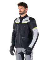 Veste Alpinestars Bogotá Pro Drystar®, veste de moto adventure touring, noir, gris glace et jaune fluo, portée par un homme avec un pantalon gris assorti et des gants noirs, dotée de panneaux de ventilation techniques et d'une conception multi-poches.