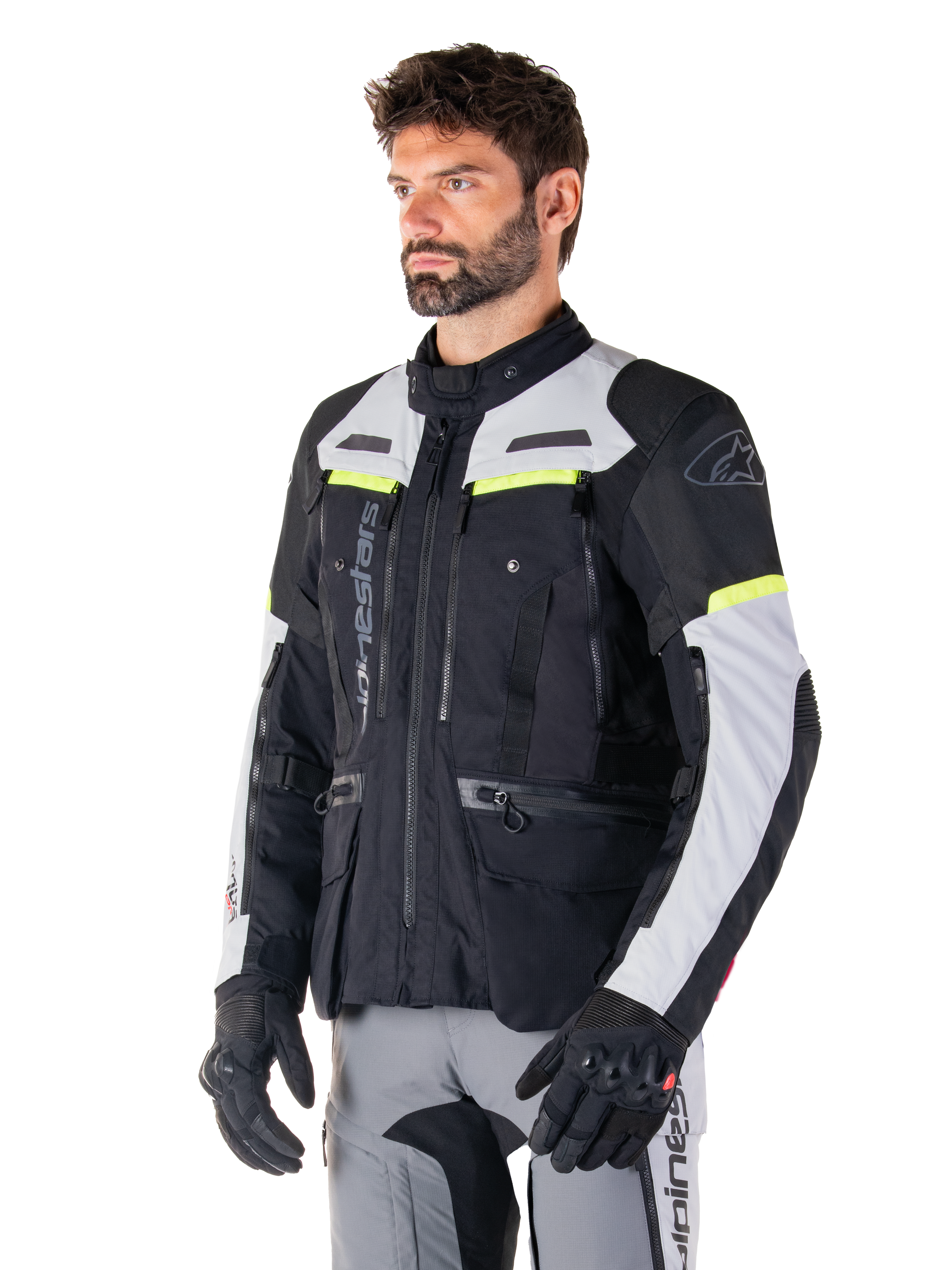 Veste Alpinestars Bogotá Pro Drystar®, veste de moto adventure touring, noir, gris glace et jaune fluo, portée par un homme avec un pantalon gris assorti et des gants noirs, dotée de panneaux de ventilation techniques et d'une conception multi-poches.