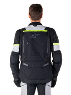 Veste Alpinestars Bogota' Pro Drystar®, veste de moto Adventure Touring, noir, gris glace et jaune fluo, vue arrière montrant le marquage « TECH TOURING » sur une bande jaune fluo, un large panneau de ventilation dorsal et des sangles de réglage à la taille, équipement technique toutes saisons