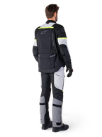 Vue arrière d'un pilote portant la veste Alpinestars Bogotá Pro Drystar® en Black Ice Gray Yellow Fluo, associée à un pantalon de touring aventure assorti, avec une grande poche arrière et des accents jaune fluo, équipement moto textile toutes saisons.