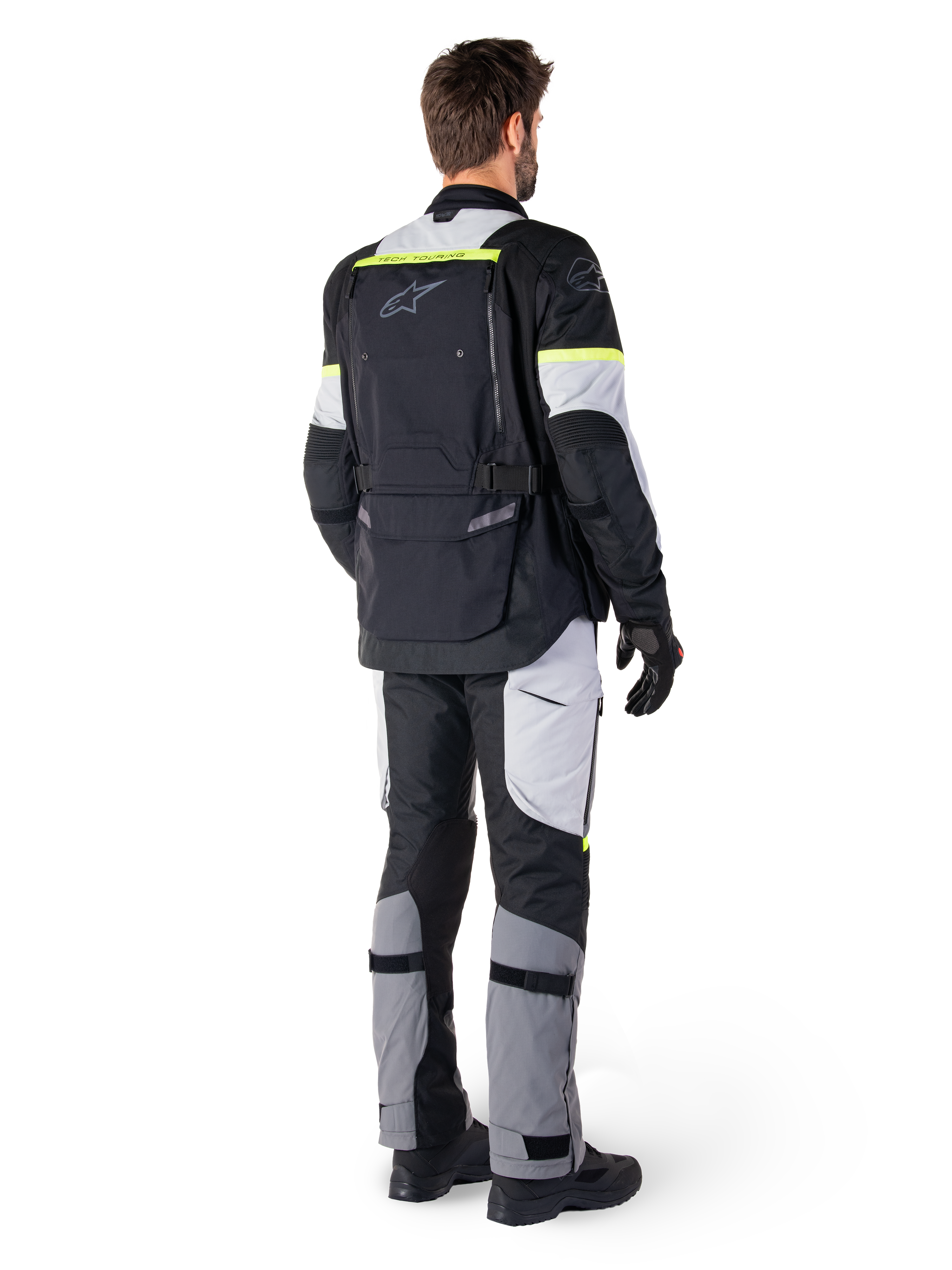 Vue arrière d'un pilote portant la veste Alpinestars Bogotá Pro Drystar® en Black Ice Gray Yellow Fluo, associée à un pantalon de touring aventure assorti, avec une grande poche arrière et des accents jaune fluo, équipement moto textile toutes saisons.