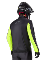 Veste Alpinestars Bogotá Pro Drystar®, vue arrière, noire avec manches jaune fluo, portée par un pilote avec un casque et des gants noirs, équipement de moto d'aventure touring haute visibilité avec une finition en textile technique.