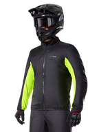 Doublure imperméable Alpinestars Bogotá Pro Drystar®, noire avec des accents jaune fluo éclatants sur les manches, portée par un pilote avec un casque et un masque noirs, équipement de moto technique.