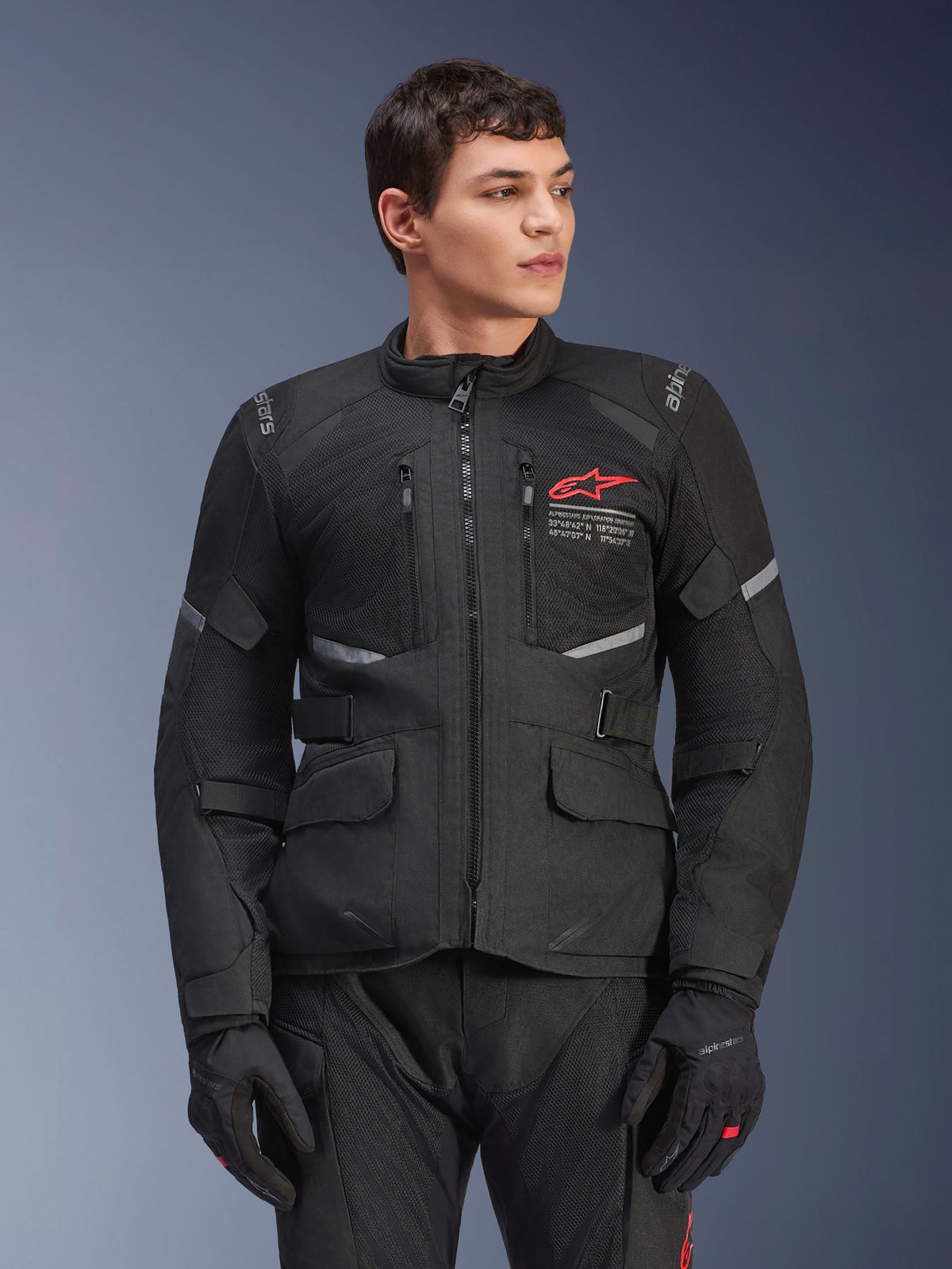 Veste Alpinestars Andes Air Drystar®, veste de moto touring noire, logo étoile rouge sur la poitrine, avec panneaux de ventilation en mesh et détails réfléchissants, portée par un mannequin homme avec des gants de moto noirs, équipement d'aventure deux saisons