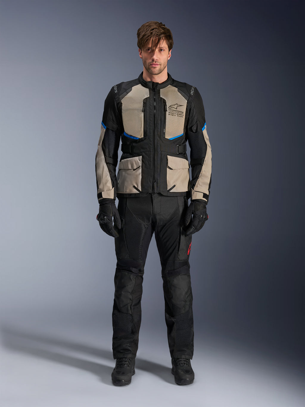 Modèle portant la veste Alpinestars Andes Air Drystar®, veste de moto touring, noir gris laurel et bleu vif, associée à un pantalon de moto et des gants noirs assortis, dotée de larges panneaux de ventilation en maille sur la poitrine et les manches pour le touring d'aventure par temps chaud.