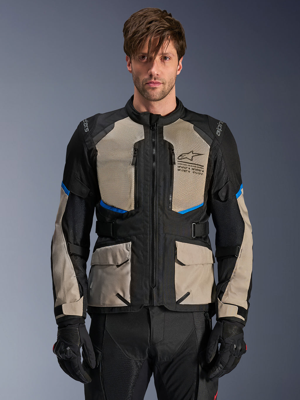 Veste Alpinestars Andes Air Drystar, veste de moto adventure touring, noir, gris laurier et bleu vif, portée par un mannequin avec des gants noirs, dotée de larges panneaux en mesh sur la poitrine pour la circulation de l'air, de poches cargo à l'avant et d'accents bleus, équipement de protection de touring