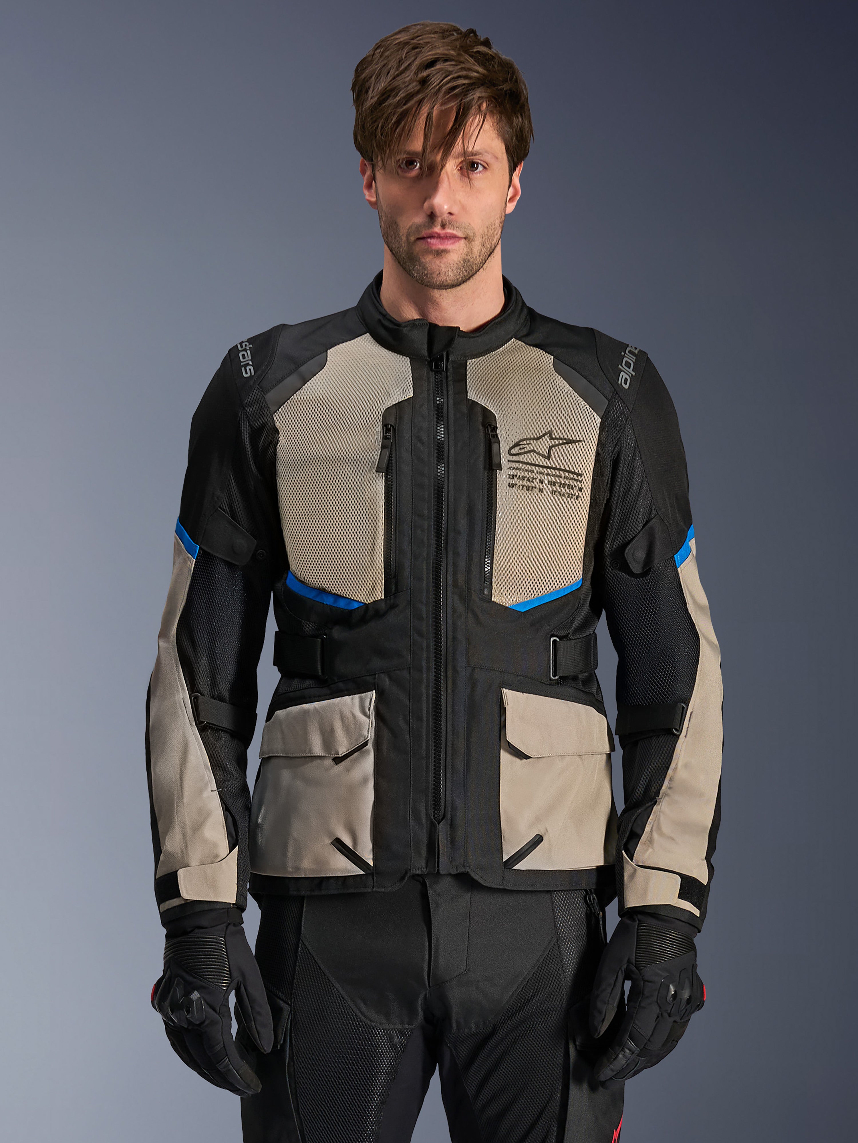 Veste Alpinestars Andes Air Drystar, veste de moto adventure touring, noir, gris laurier et bleu vif, portée par un mannequin avec des gants noirs, dotée de larges panneaux en mesh sur la poitrine pour la circulation de l'air, de poches cargo à l'avant et d'accents bleus, équipement de protection de touring