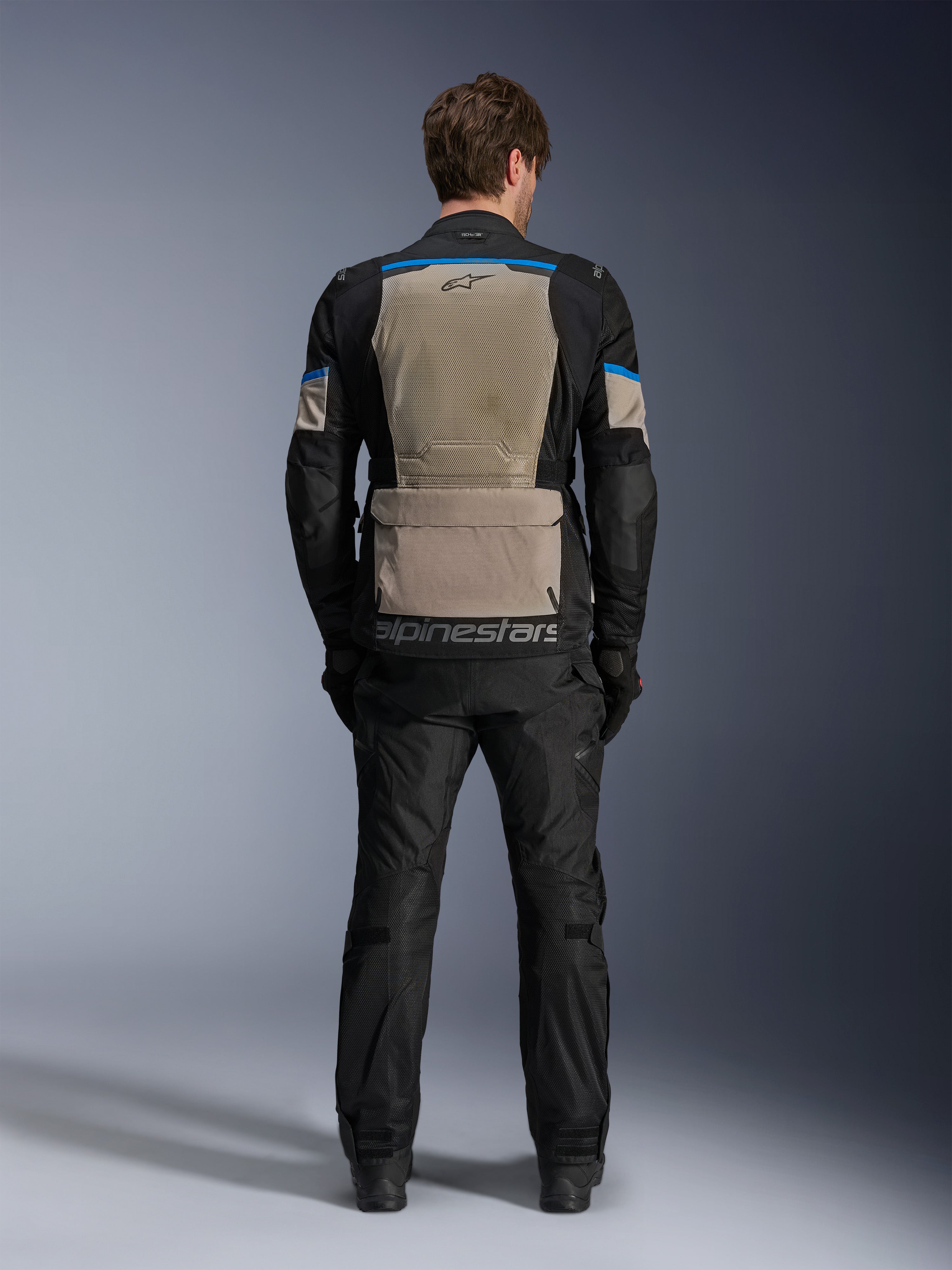 Veste Alpinestars Andes Air Drystar®, Noir, Gris Laurel et Bleu Éclatant, vue arrière montrant un large panneau de ventilation en maille, grande poche de rangement au bas du dos avec marquage Alpinestars, veste de touring moto technique portée avec un pantalon assorti.