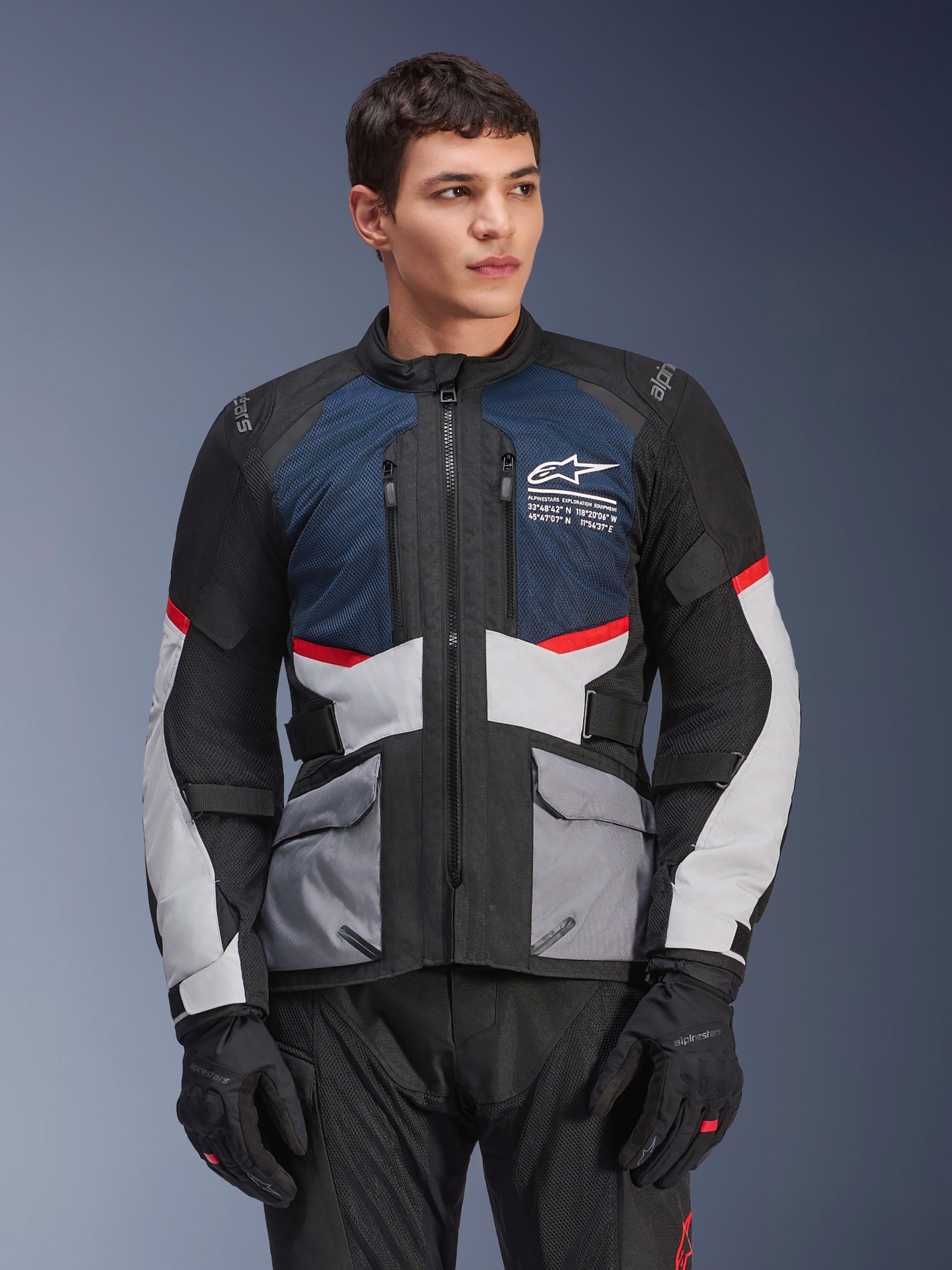 Veste Alpinestars Andes Air Drystar®, veste de moto touring, bleu profond, noir et gris glace avec des accents rouges, portée par un mannequin homme avec des gants noirs, dotée de panneaux de ventilation en maille et de poches utilitaires à l'avant, équipement moderne de route et d'aventure