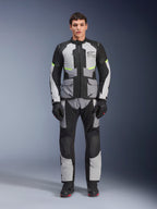 Veste Alpinestars Andes Air Drystar® en Gris Glacé, Gris Foncé et Noir, portée par un modèle masculin avec pantalon et gants de moto assortis, design touring aventure avec de grandes poches avant et des accents jaune fluo, vue de face en studio