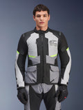 Motard portant la veste Alpinestars Andes Air Drystar® en gris glacier, gris foncé et noir, avec des accents jaune fluo et des panneaux de ventilation en mesh, accompagnée d'un pantalon et de gants de moto assortis, équipement de touring aventure