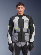 Motard portant la veste Alpinestars Andes Air Drystar® en gris glacier, gris foncé et noir, avec des accents jaune fluo et des panneaux de ventilation en mesh, accompagnée d'un pantalon et de gants de moto assortis, équipement de touring aventure