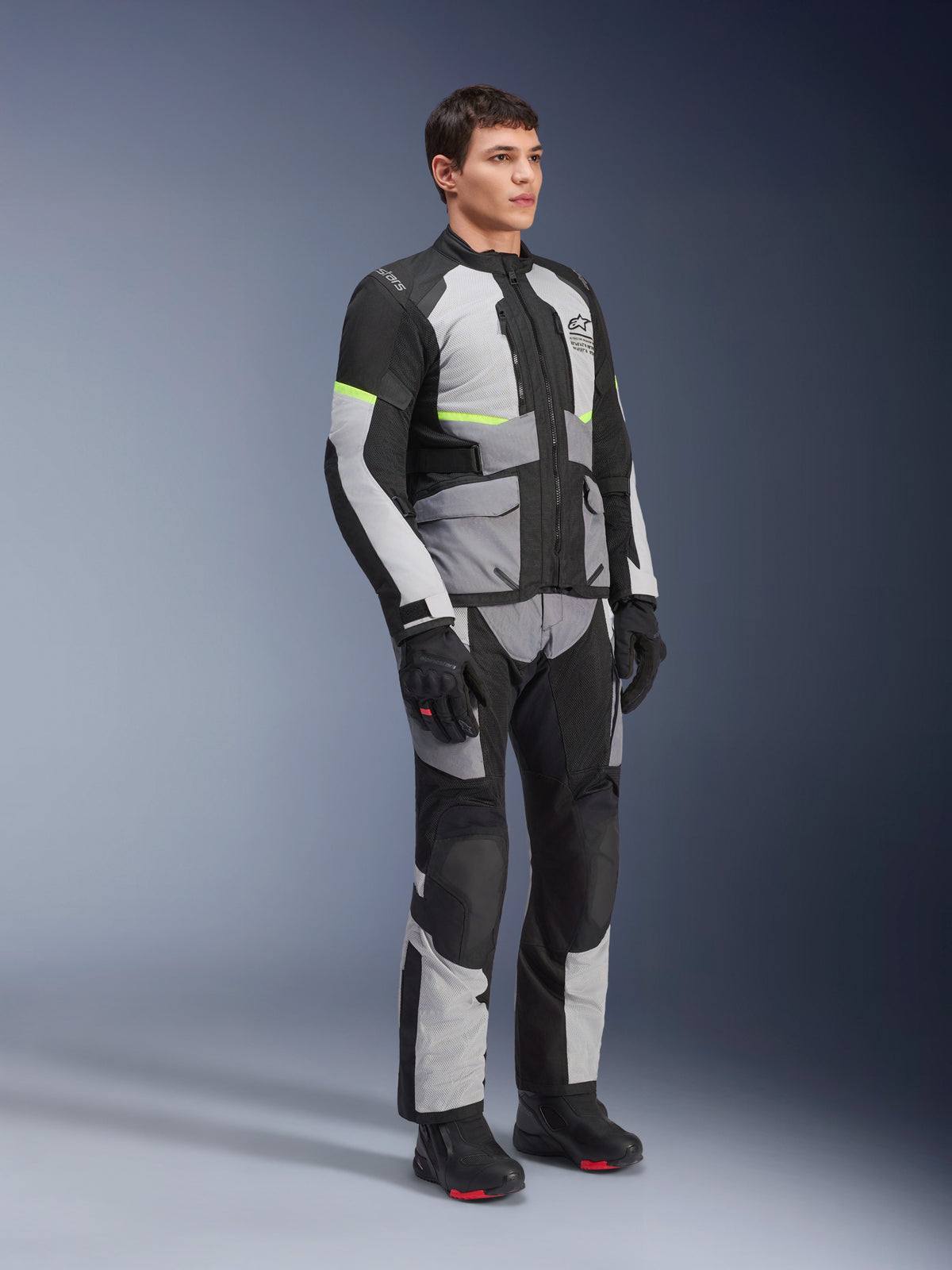 Alpinestars Andes Air Drystar® Jacket, Ice Gray, Dark Gray and Black, worn by a model in a full adventure touring outfit with matching pants and black boots, featuring mesh ventilation, neon accents, and Alpinestars branding.