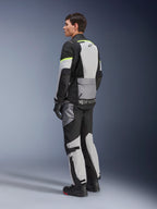 Motard portant une veste et un pantalon Alpinestars Andes Air Drystar®, équipement de touring aventure en Ice Gray Dark Gray Black avec des accents jaune fluo, doté de larges panneaux en mesh pour la circulation de l'air, logo Alpinestars au dos, porté avec des gants et des bottes noirs.