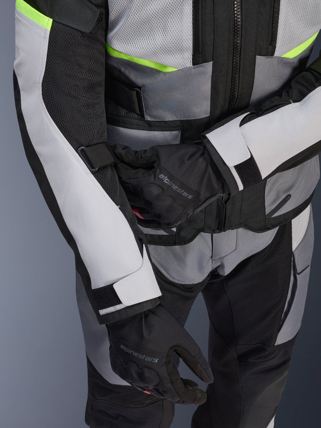 Veste Alpinestars Andes Air Drystar®, veste de touring moto, gris glace et gris foncé avec des accents jaune fluo, gros-plan montrant les panneaux en mesh et les sangles de réglage, portée avec des gants Alpinestars noirs